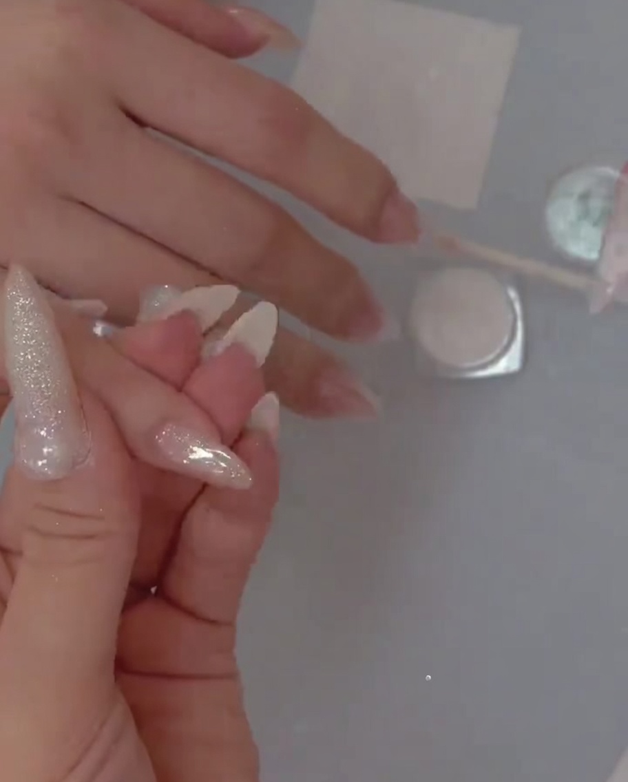 Un pinceau de détail déposant délicatement des paillettes fines sur la base gel de longle.