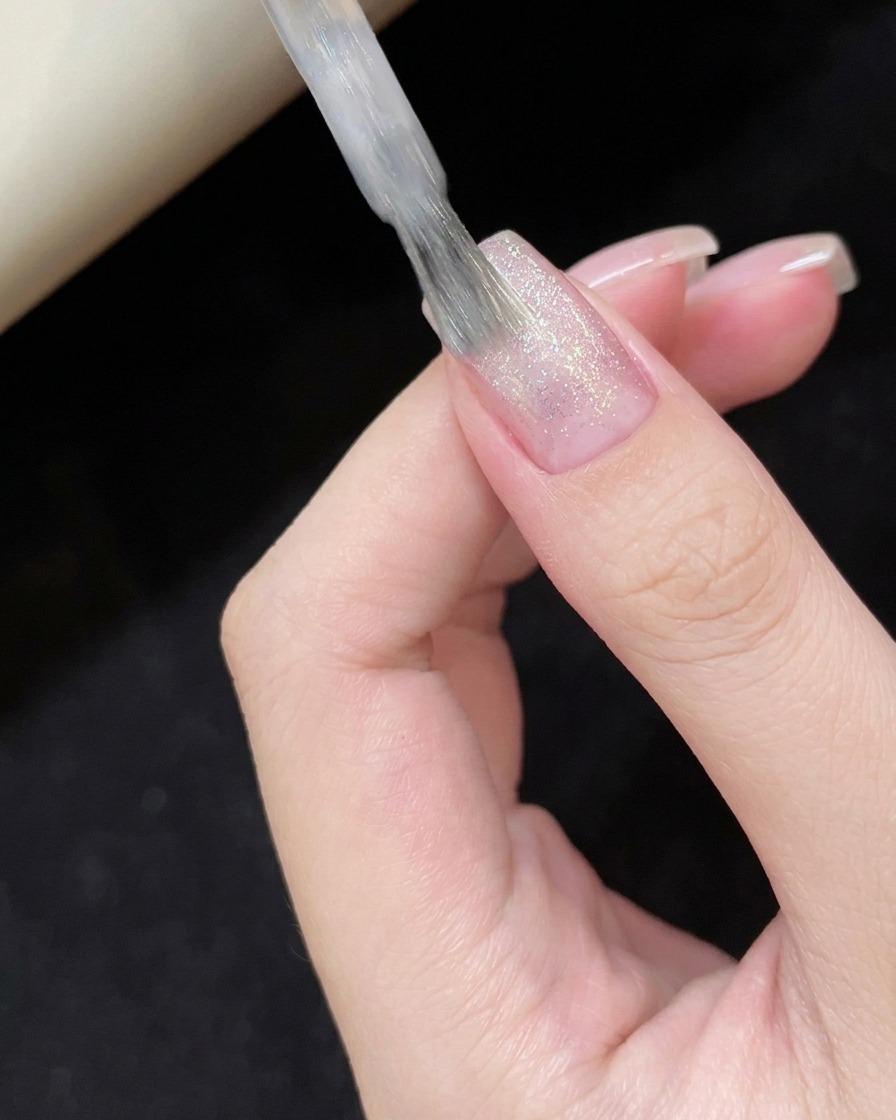 Application dun vernis cat-eye blanc translucide sur la surface de longle.