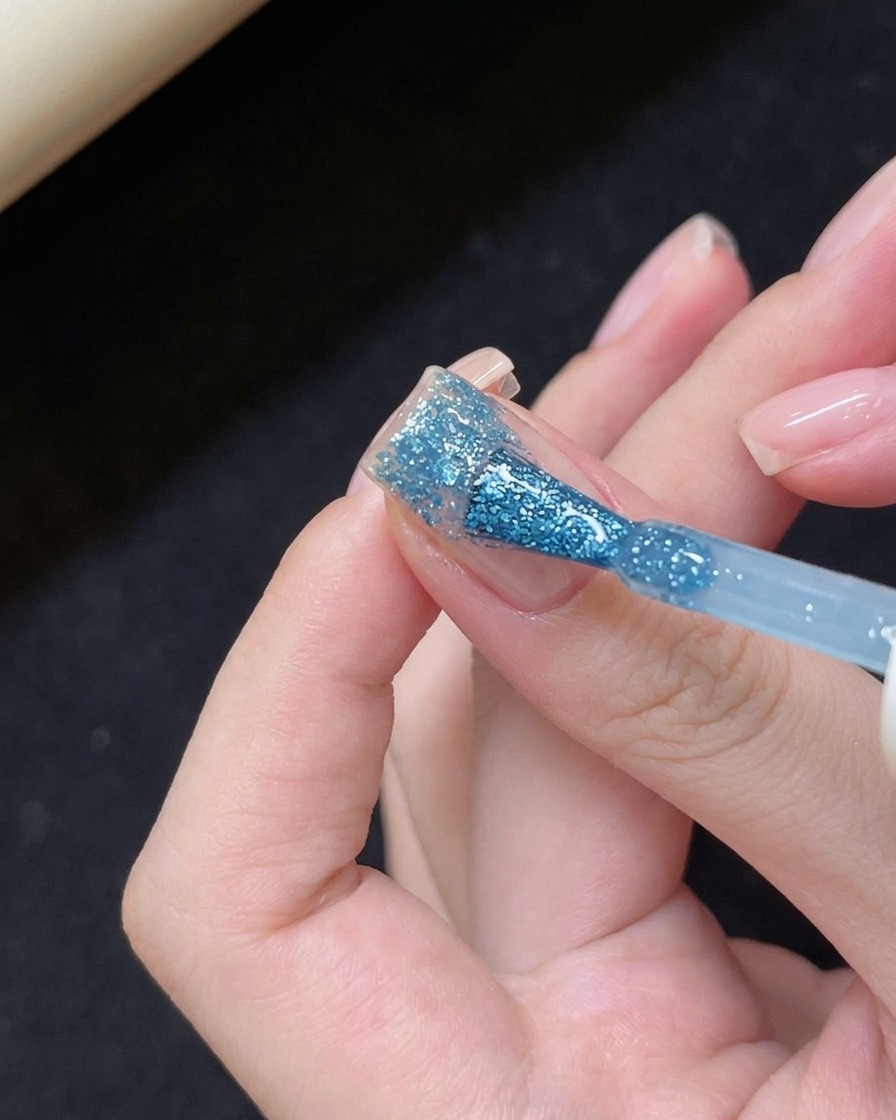 Application de gel teinté bleu sur le bout de longle.
