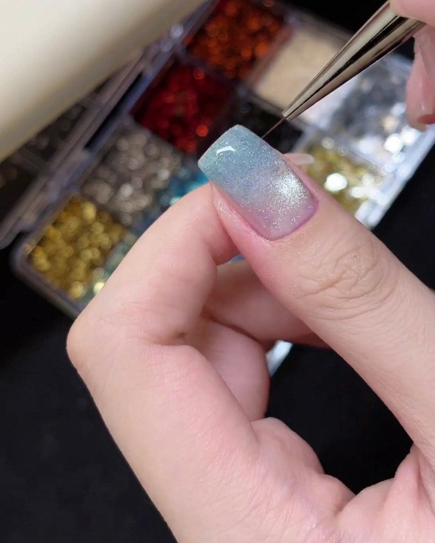 Une pince déposant une petite étoile à paillettes argentées sur le bout dun ongle manucuré.