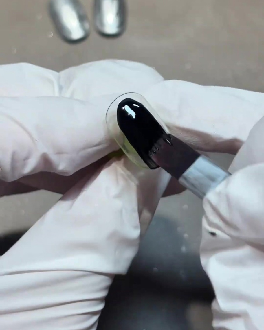 Un pinceau appliquant une couche de vernis gel noir opaque sur un ongle.