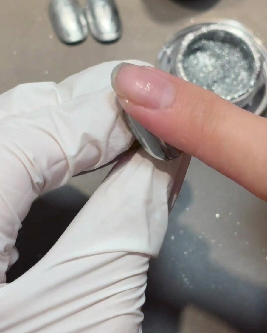 Application dune couche de gel de renforcement transparent sur un ongle recouvert de chrome.