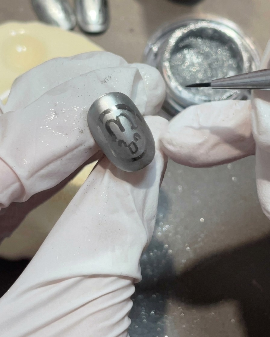Un gros plan dun pinceau liner appliquant une petite perle de gel transparent sur un ongle gris mat pour former une goutte deau.