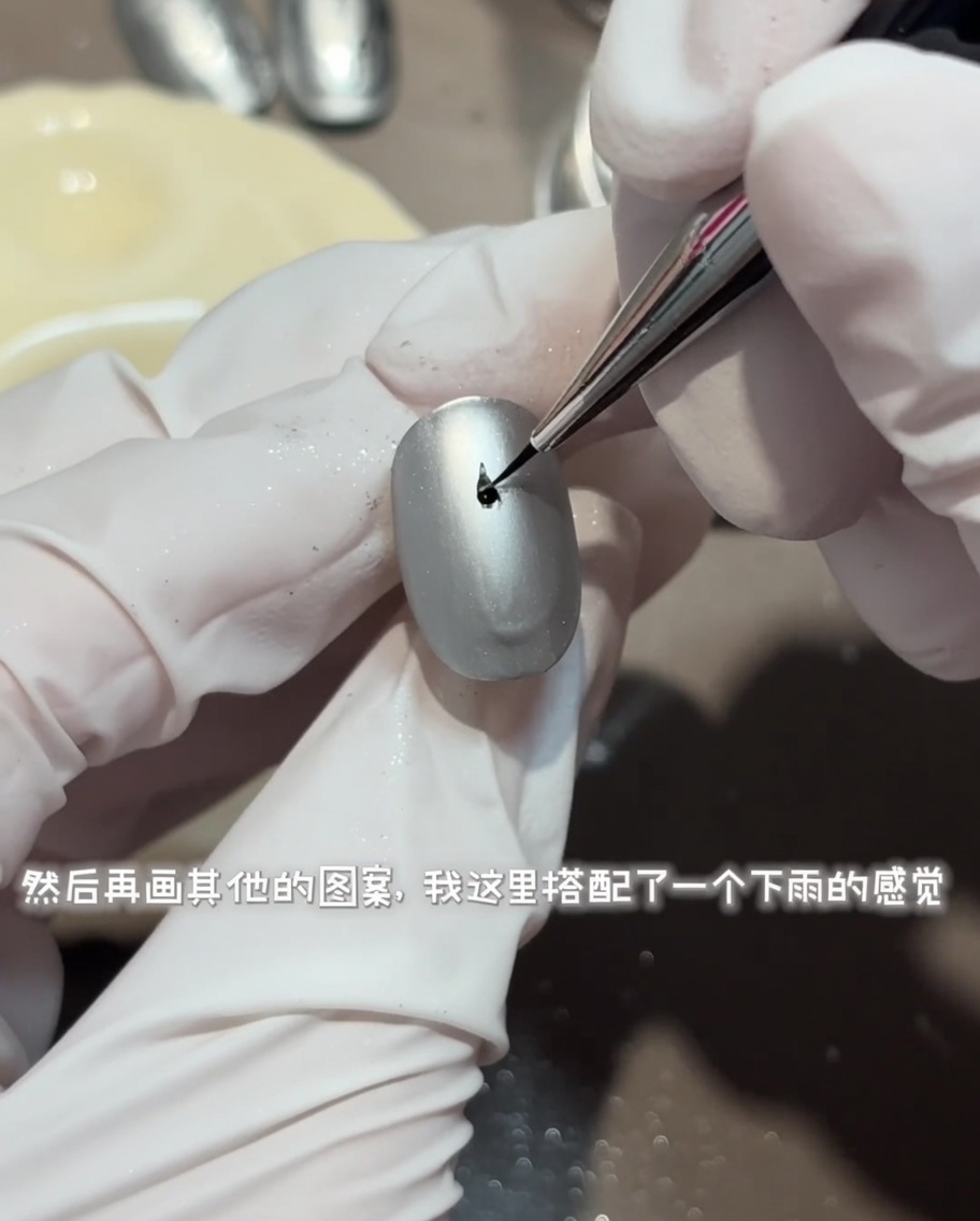 Un pinceau liner fin dessinant un motif détaillé de rides deau circulaires avec du top coat brillant sur un ongle gris mat.