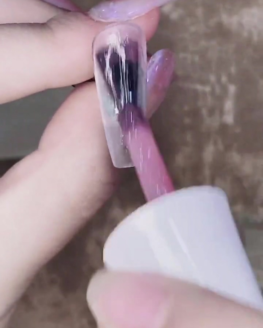 Un pinceau appliquant une deuxième couche de gel rose translucide sur la première couche catalysée.