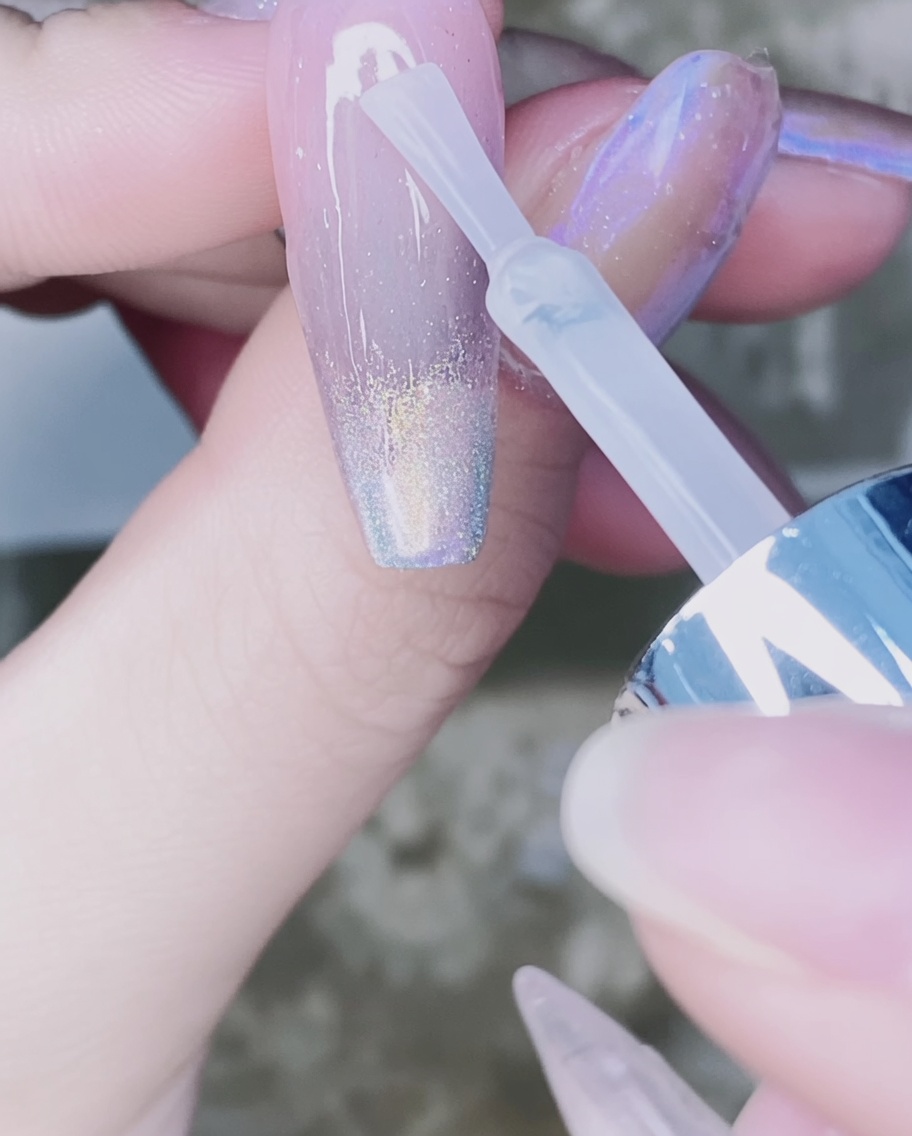 Un pinceau à ongles appliquant un top coat transparent sur le dégradé de poudre chrome de longle.