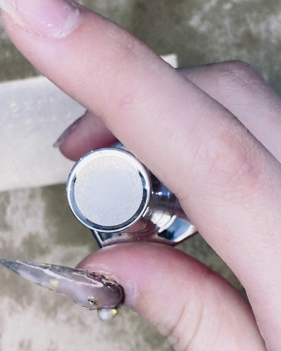 Un pinceau fin pour nail art appliquant une petite goutte de top coat autour de la base dun strass monté sur un ongle.