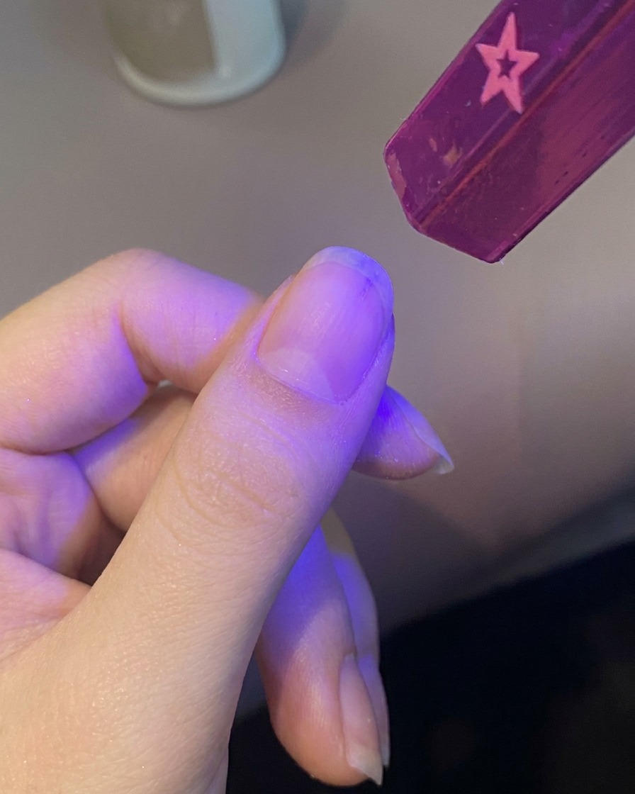 Une main plaçant un ongle sous une petite lampe UV portable violette.