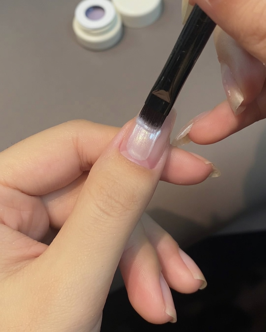 Un pinceau appliquant du vernis cat eye violet sur un ongle.