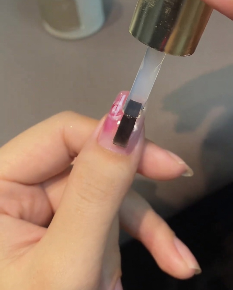 Un pinceau appliquant un top coat transparent sur le nail art.