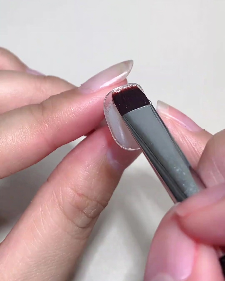 Un pinceau appliquant une couche de gel cat-eye nude sur un ongle déjà doté dune base catalysée.