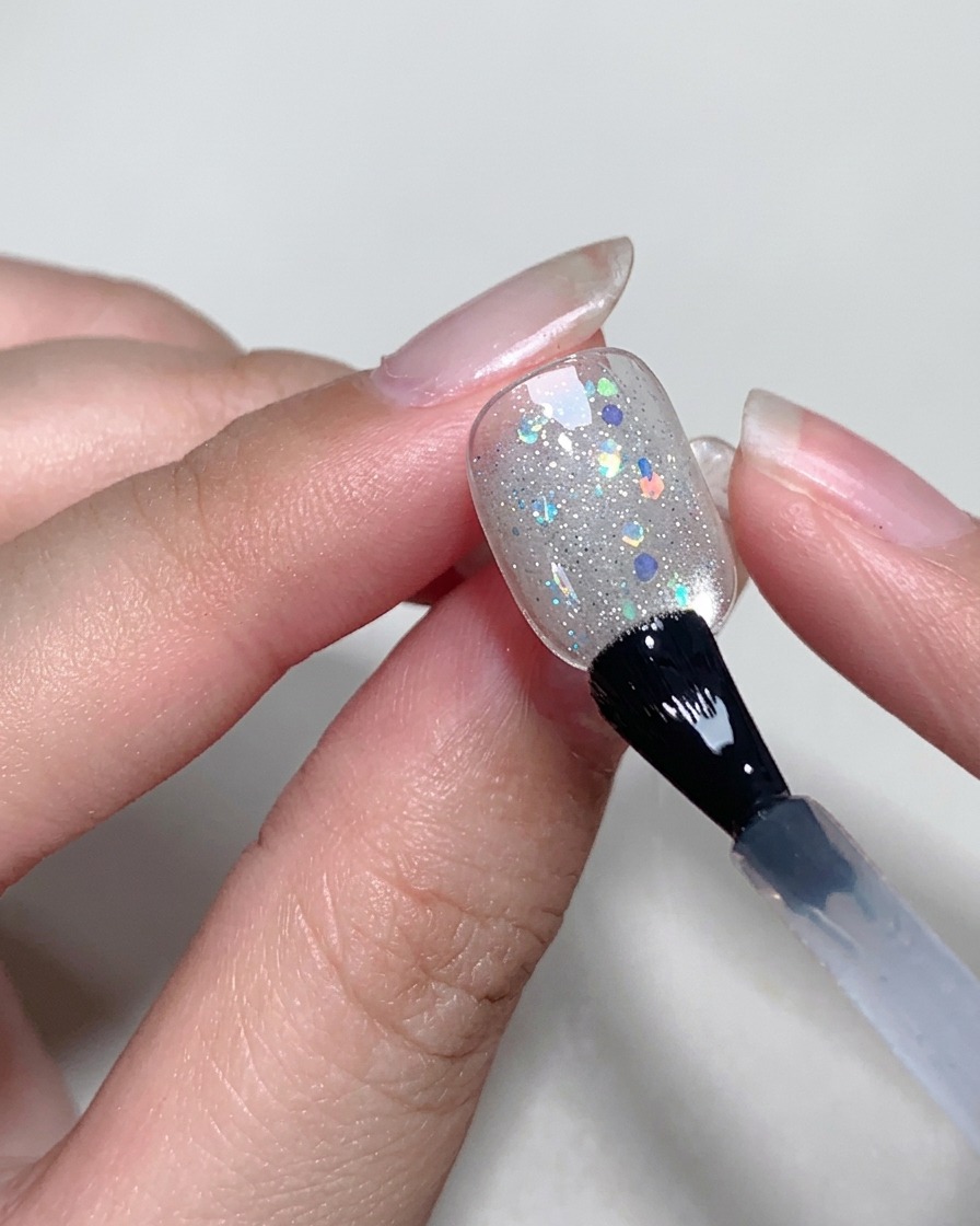 Application dune couche fine et transparente de blooming gel sur la surface de longle avec un pinceau.