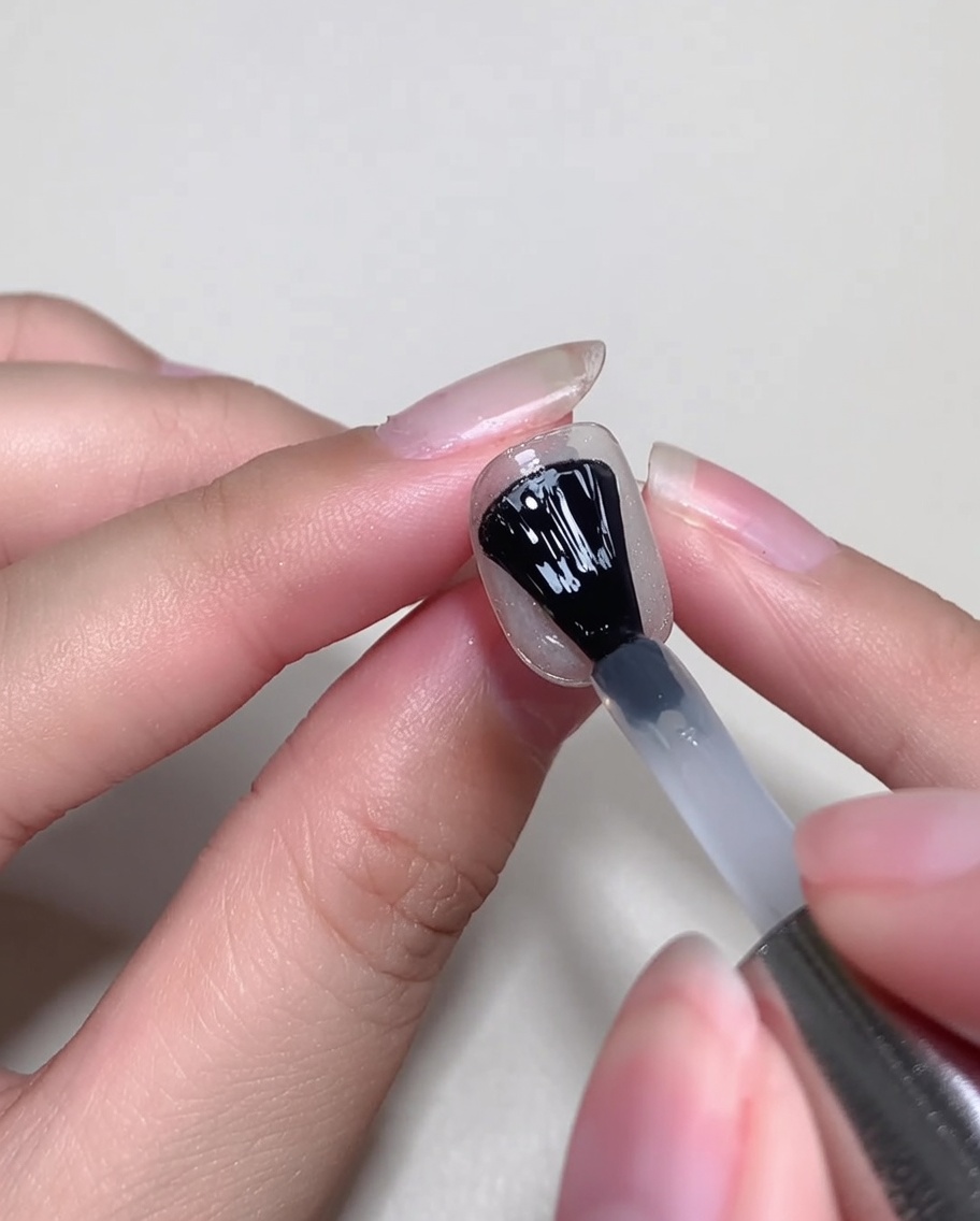 Un pinceau de vernis gel appliquant une fine couche de blooming gel transparent sur un ongle décoré.