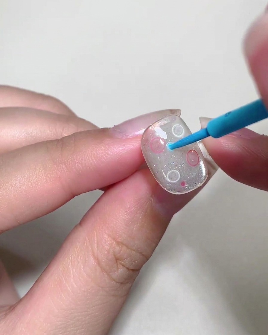 Un outil de dotting plaçant de petites bulles de liquide coloré sur la surface dun ongle.