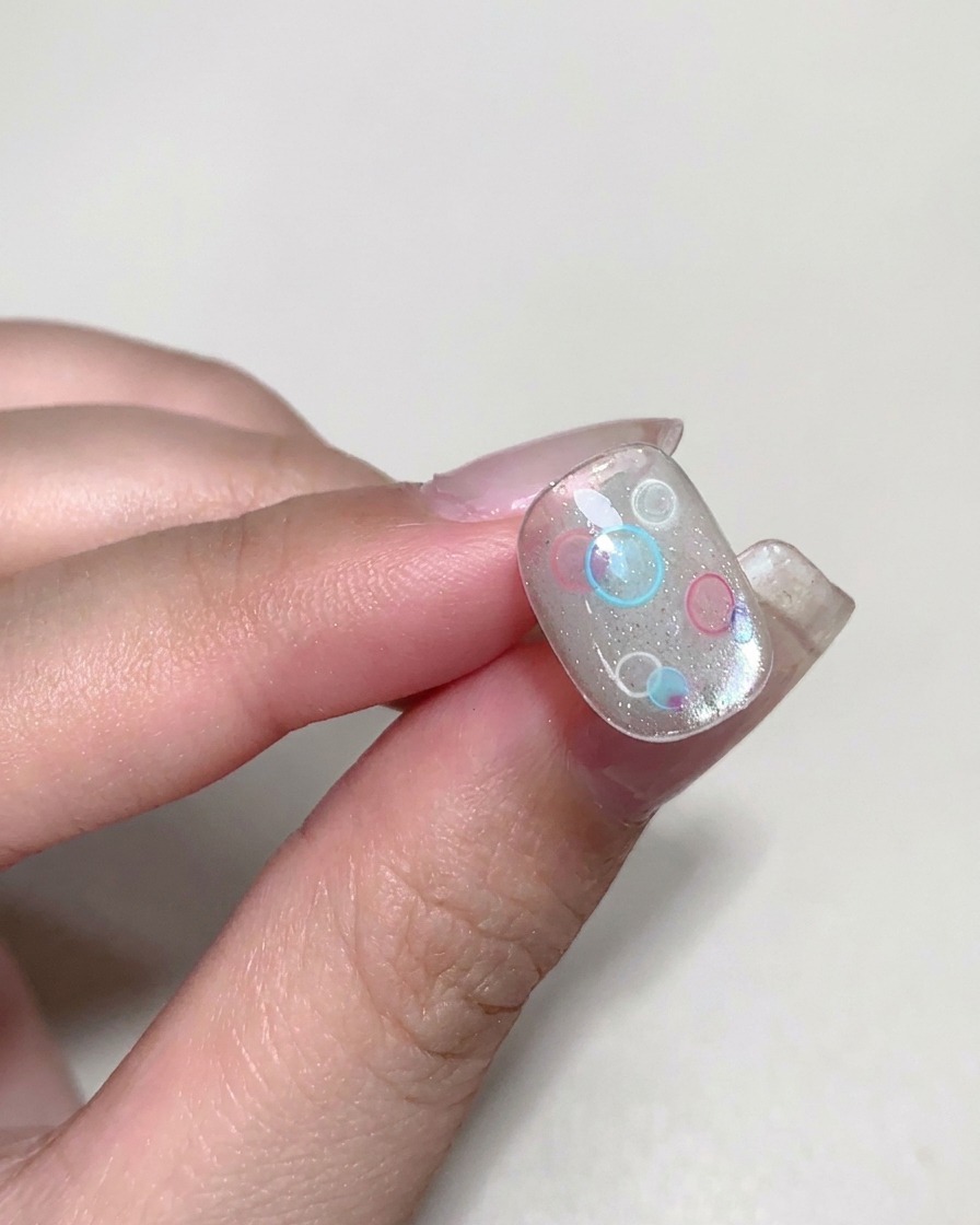 Un pinceau appliquant un gel constructeur transparent visqueux sur un ongle décoré.
