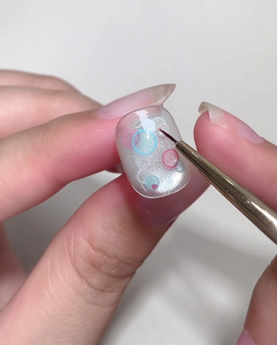 Un pinceau à pointe fine plaçant soigneusement de petits sequins circulaires transparents sur un ongle.