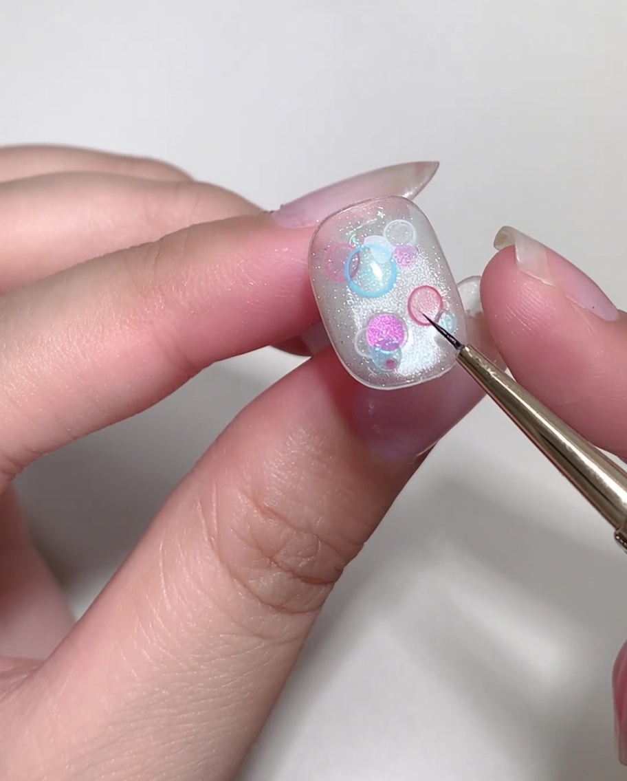Un pinceau liner fin dessinant une petite étoile en forme de croix blanche sur un ongle manucuré.