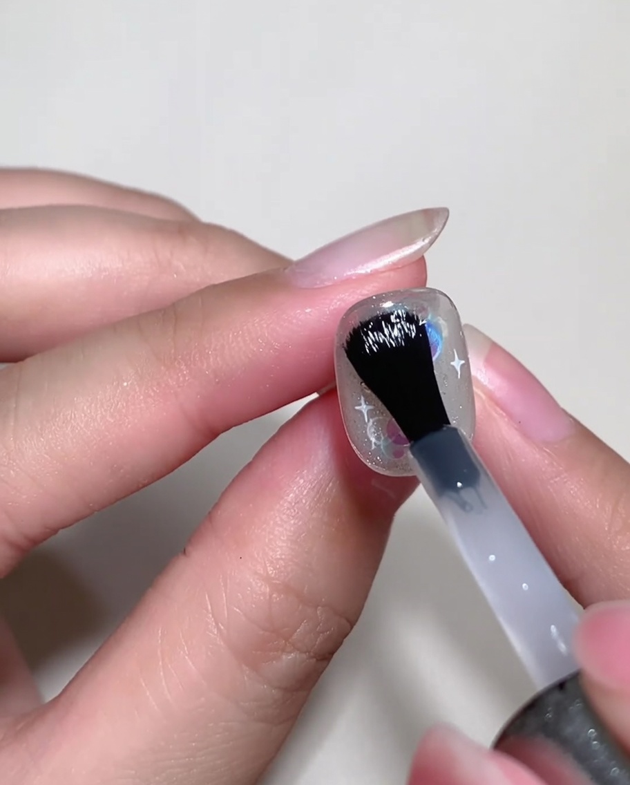 Un pinceau à ongles appliquant un gel constructeur transparent sur un ongle décoré pour niveler la surface.