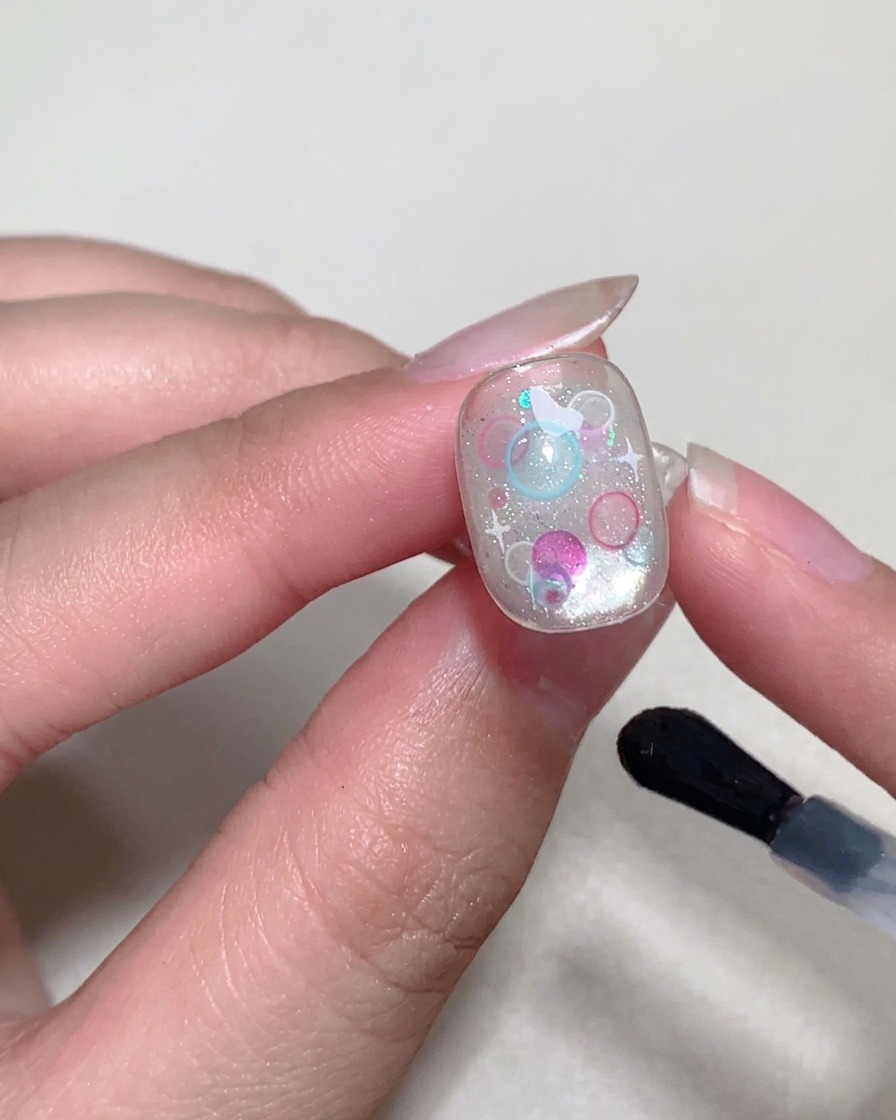 Un pinceau appliquant une couche finale de top coat brillant sur la surface de longle.