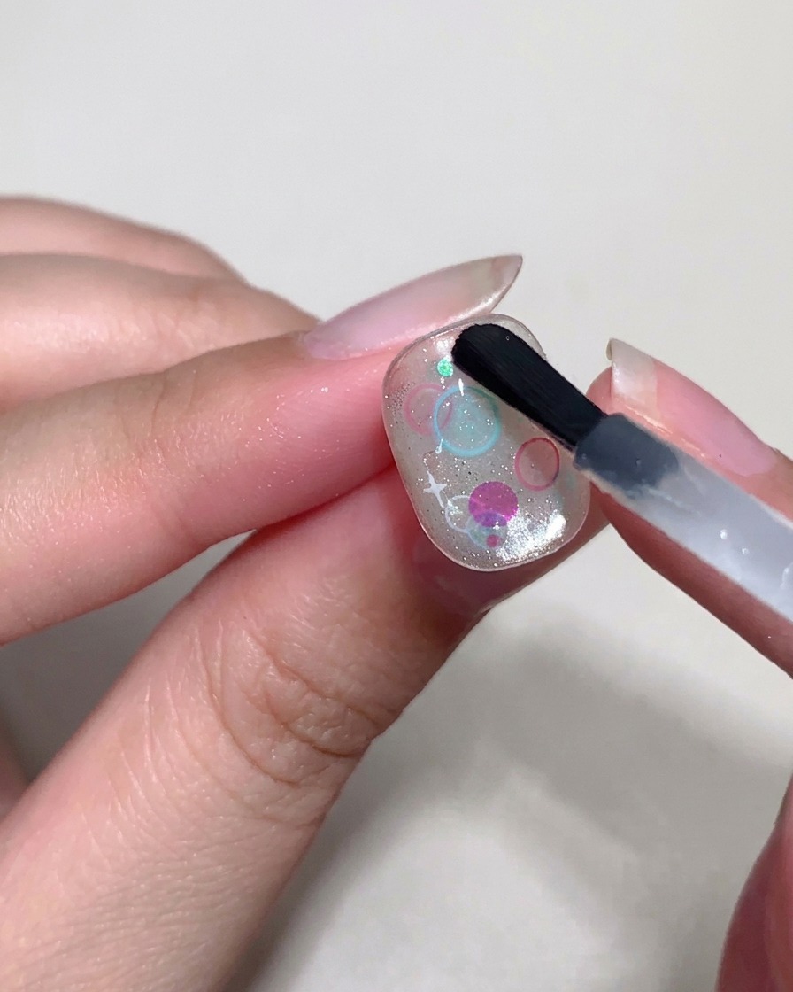 Un pinceau de précision utilisant un top coat épais pour former de petites bulles en relief sur les sequins de longle.
