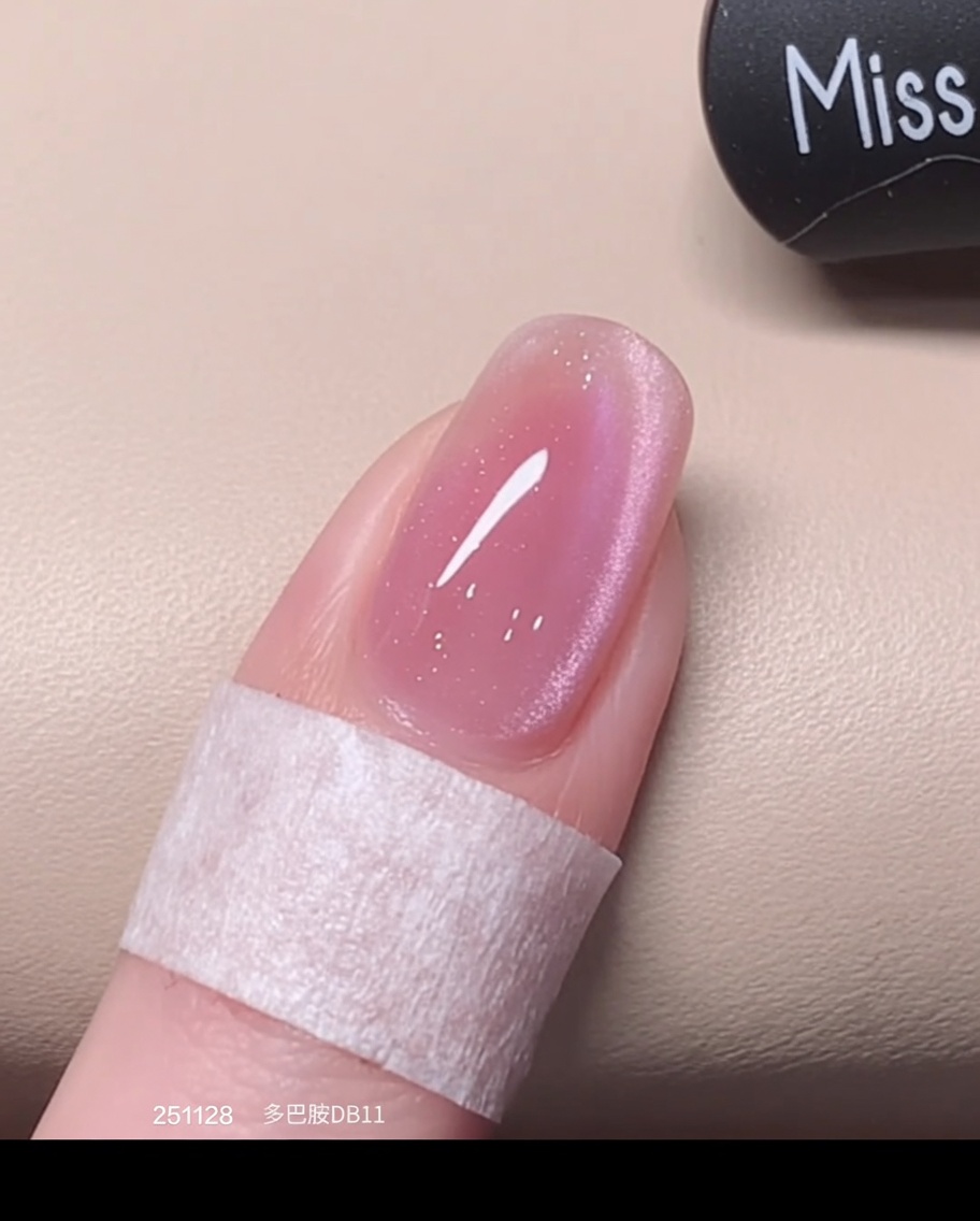 Un pinceau appliquant une seconde couche fraîche de vernis œil de chat rose sur la base préalablement catalysée.