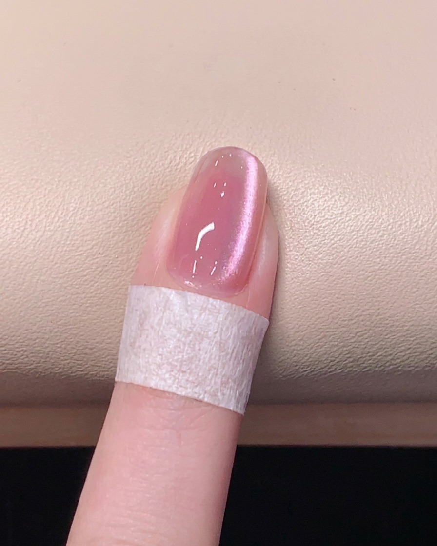 Un pinceau appliquant un top coat transparent brillant sur un ongle gel œil de chat rose.