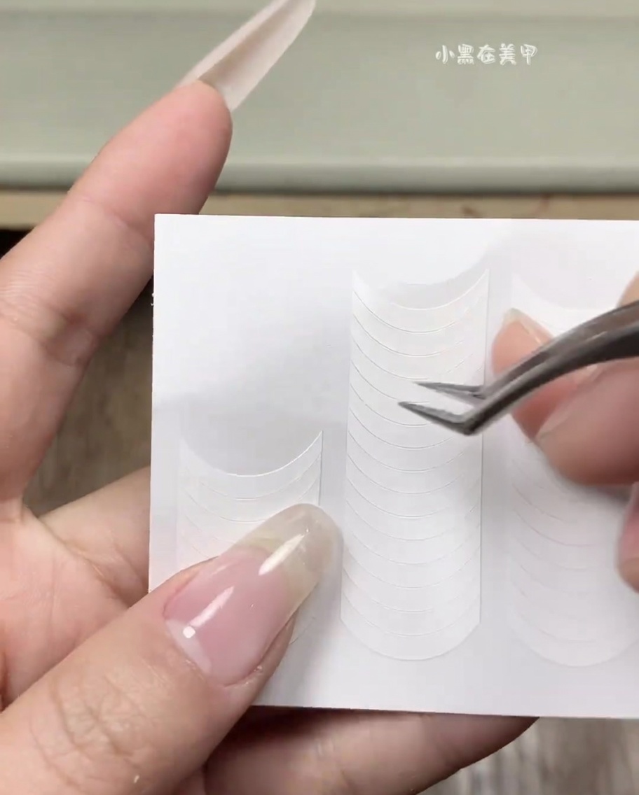 Une main appliquant un guide adhésif blanc pour French manucure sur un ongle naturel propre.