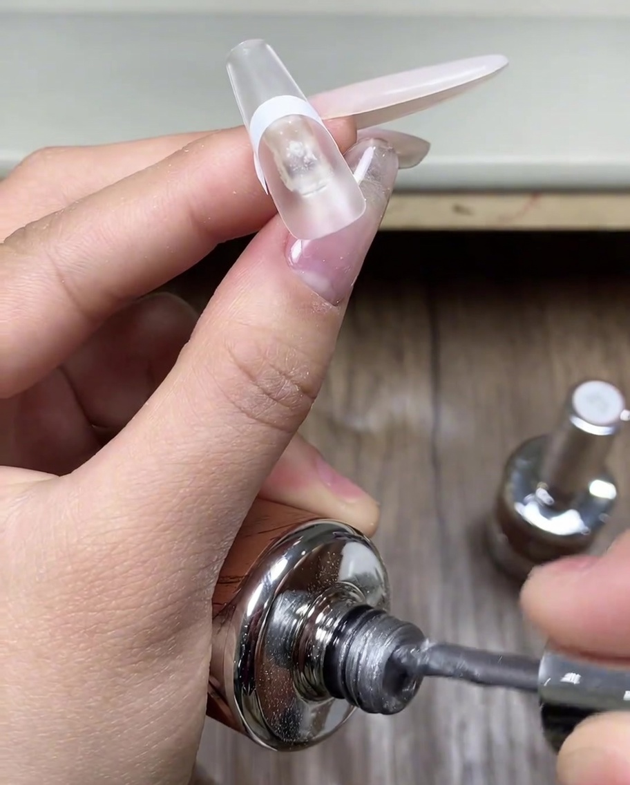 Un pinceau appliquant une couche de gel cat eye gris sur la pointe dun ongle protégé par un adhésif.