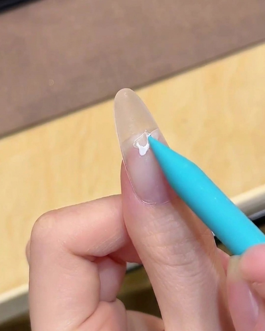 Un pinceau appliquant une base coat gel transparente sur un ongle propre et nu.