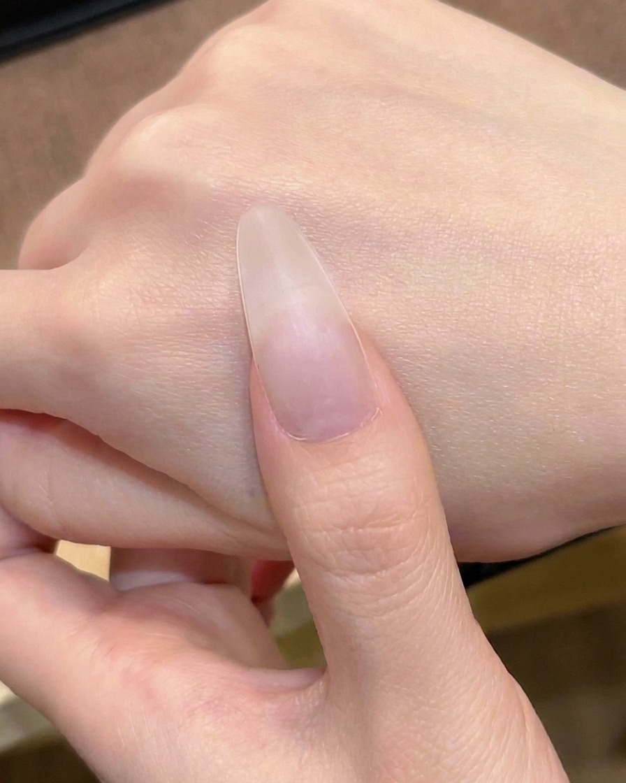 La première couche de gel rose nude transparent étant appliquée sur longle avec un pinceau à vernis.