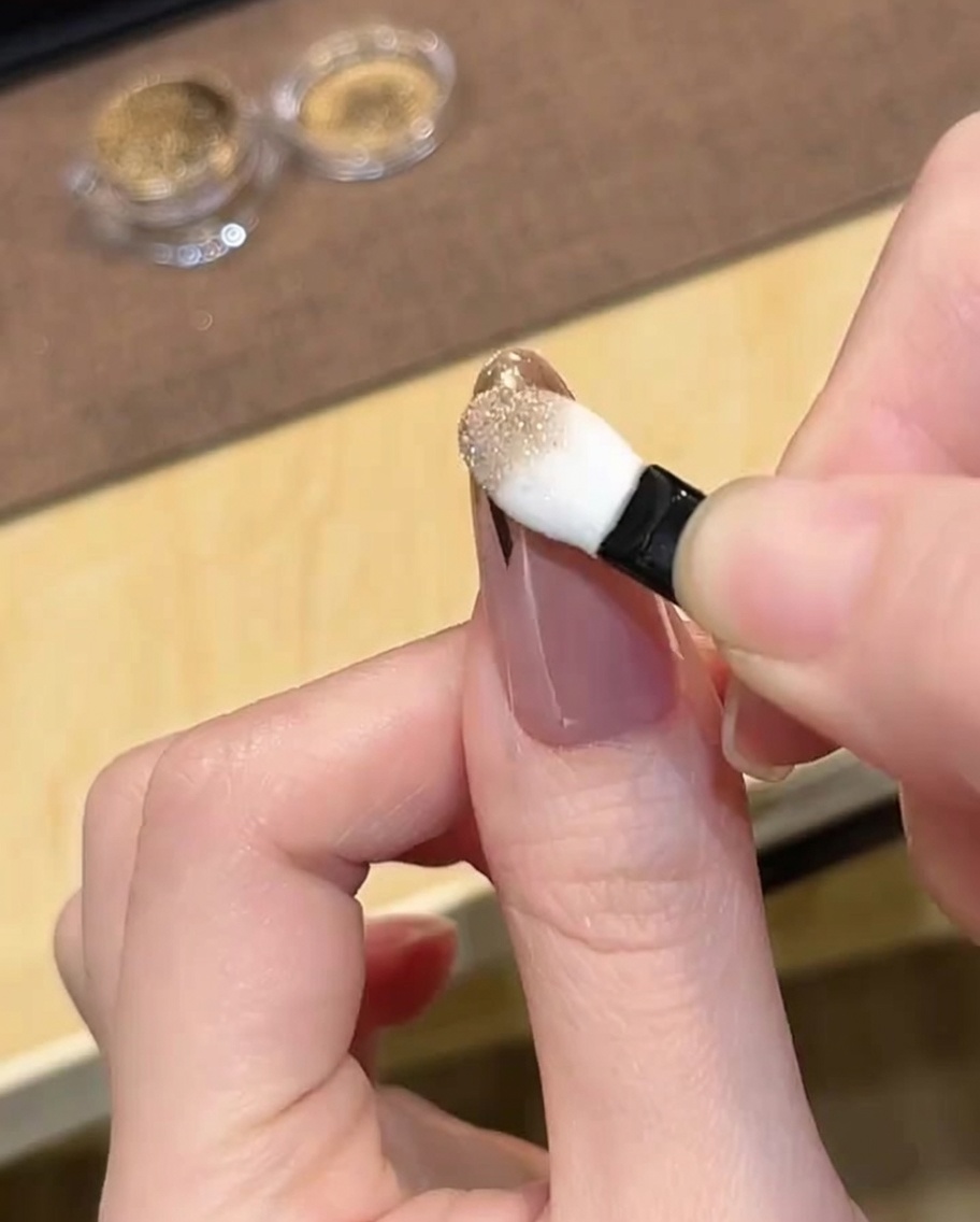 Un applicateur éponge pour fard à paupières frottant de la poudre chrome doré sur le bout dun ongle avec guide.