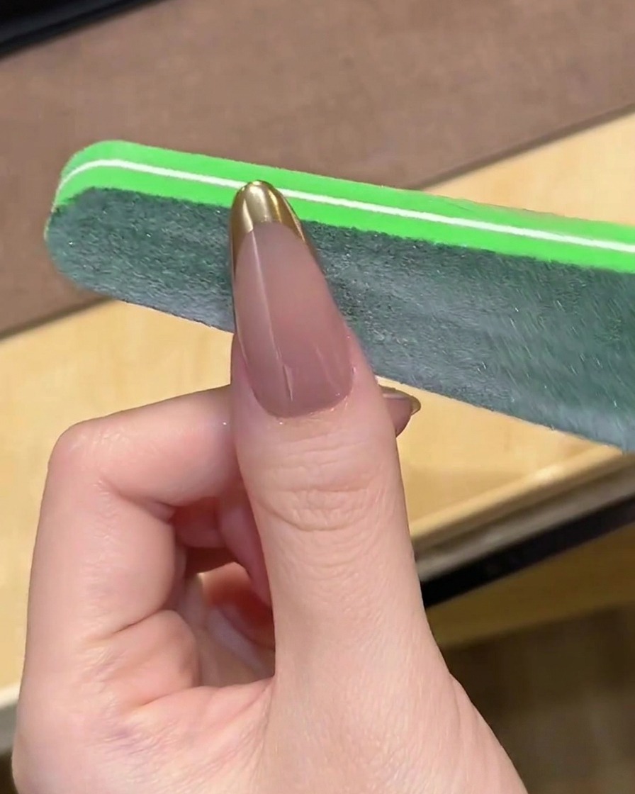 Une lime à ongles lissant doucement le bout dune manucure French chromée.