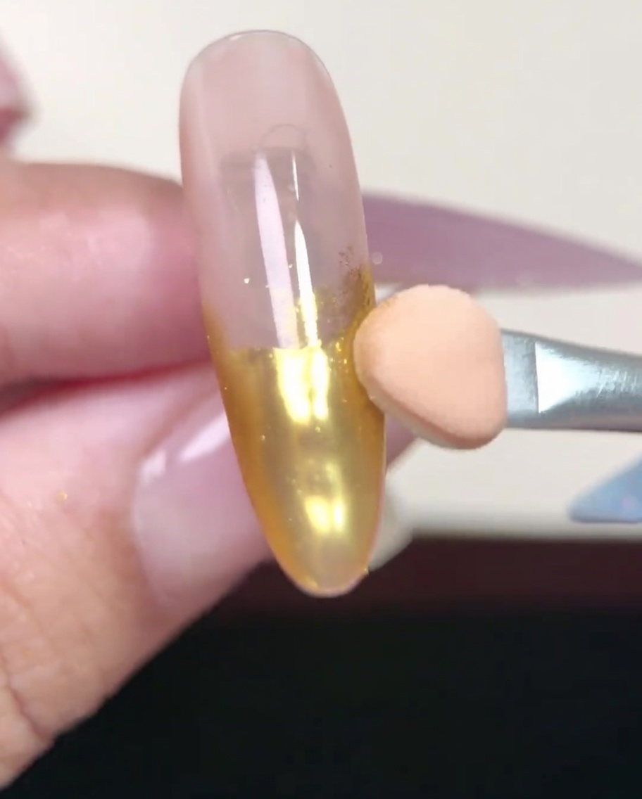 Pinceau appliquant une couche de gel base nude sur un ongle en amande.