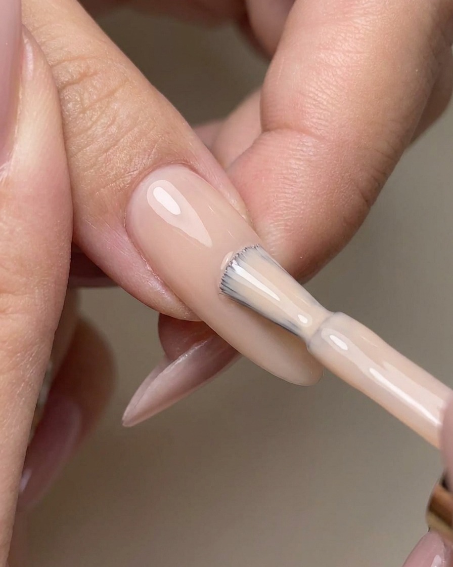 Pinceau appliquant un top coat transparent sans résidu sur un ongle nude.