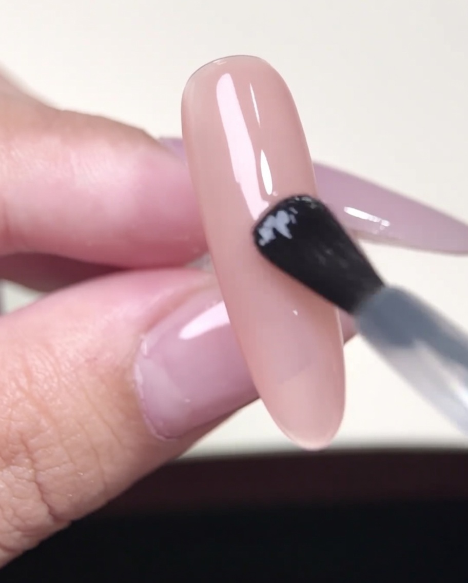 Une pince déposant un sticker guide French sur un ongle nude.
