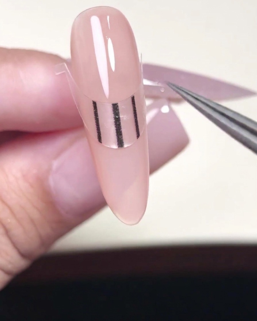Un outil métallique pressant les bords dun sticker French sur un ongle.