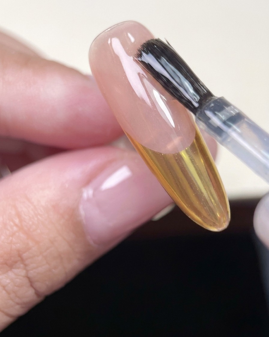 Pinceau appliquant un top coat brillant sur un ongle avec une French chrome or.