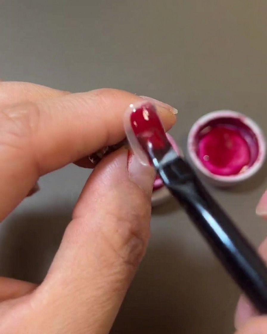 Gros plan dun pinceau appliquant un gel rouge profond sur longle.