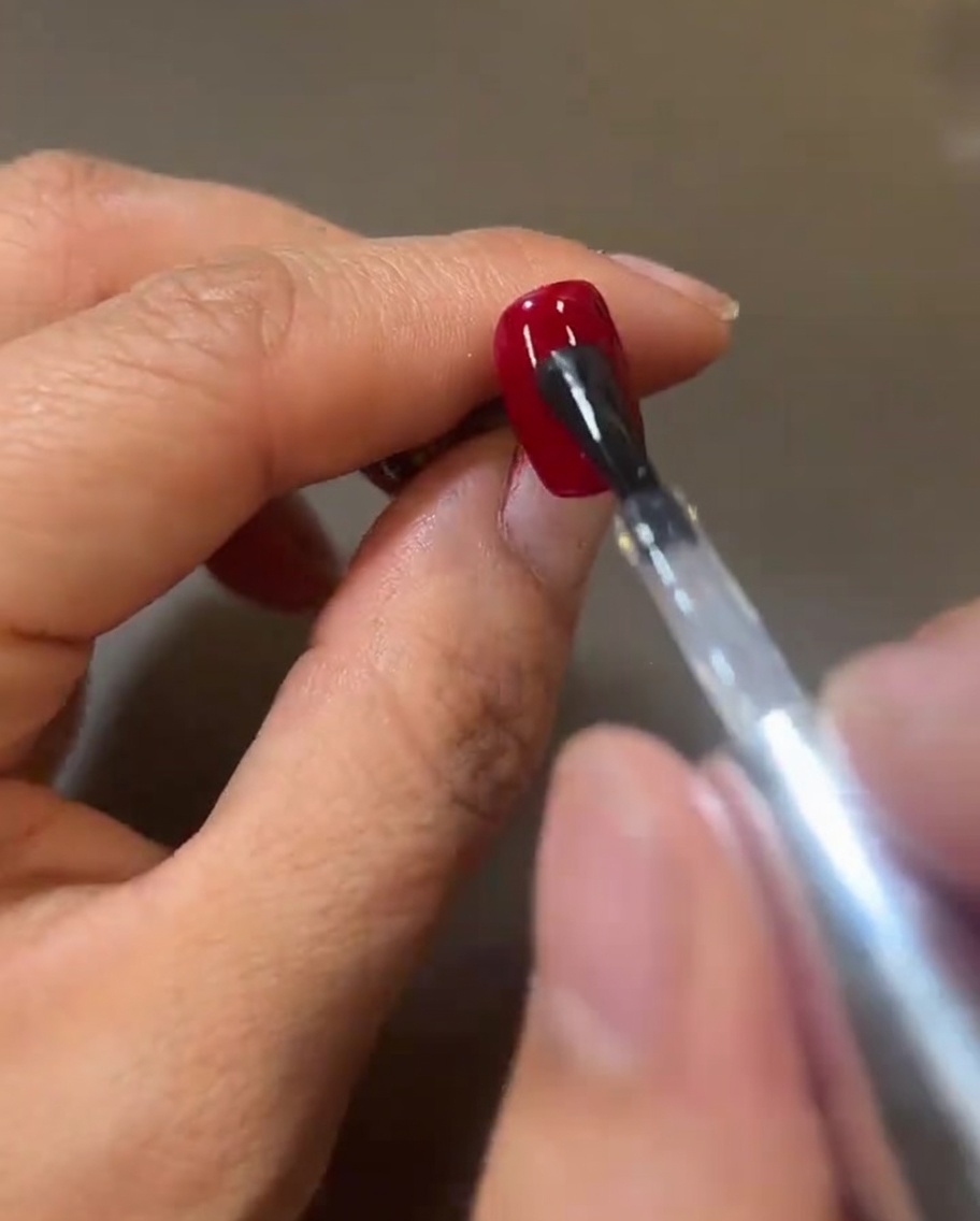 Un pinceau déposant une couche de top coat brillant sur le gel rouge.