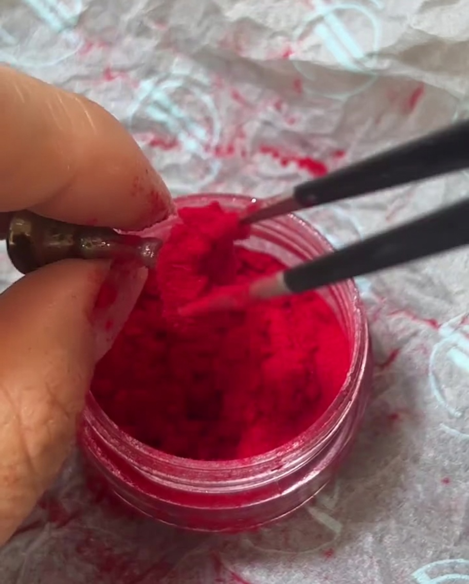 Pinces métalliques au-dessus dun pot de poudre velours rouge, saisissant quelques fibres.
