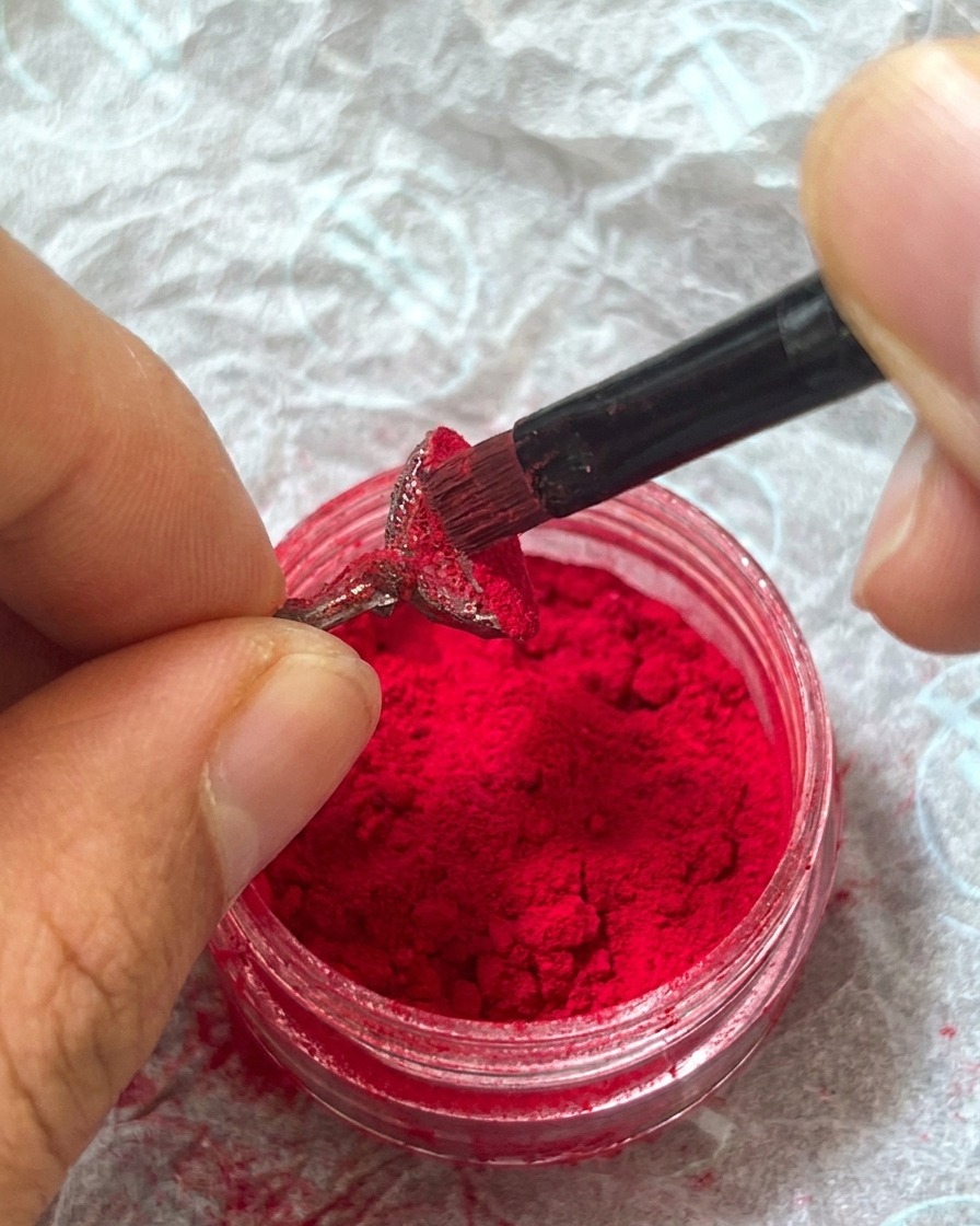 Un doigt tapotant doucement la poudre rouge sur longle pour la fixer dans le gel.