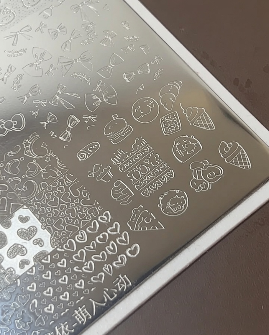 Pinceau appliquant un vernis blanc épais sur des motifs alimentaires sur une plaque en métal.
