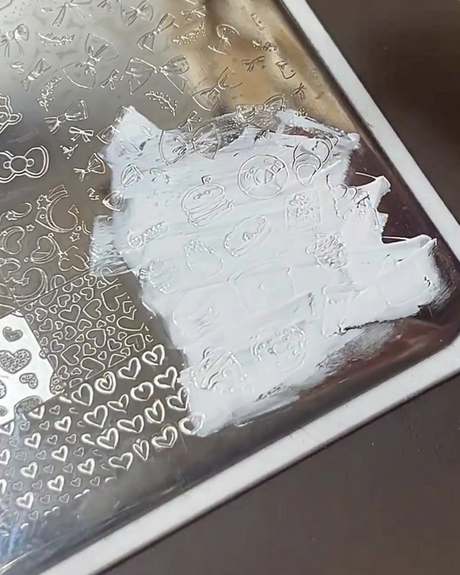 Carte racloir passant sur la plaque de stamping, laissant les motifs remplis de vernis blanc.