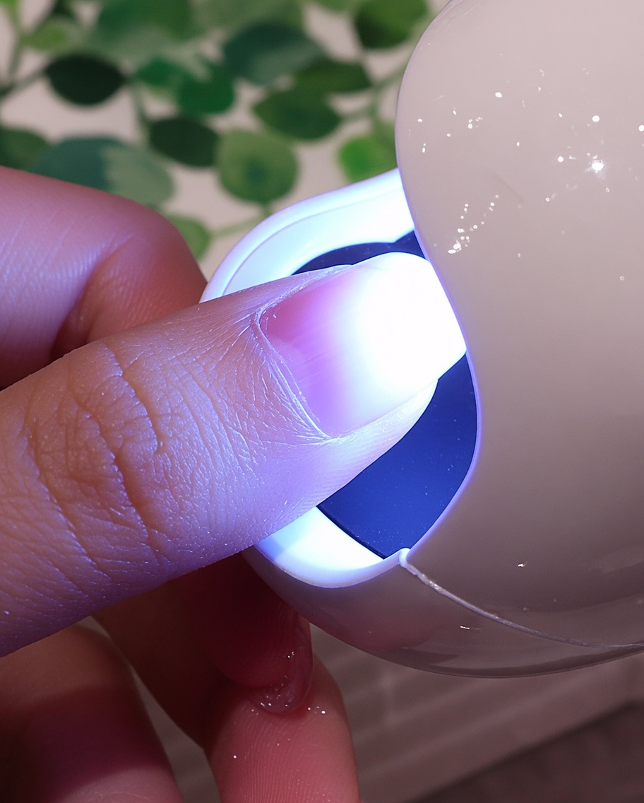 Un ongle recouvert dune texture blanche sous la lumière violette dune petite lampe UV/LED.