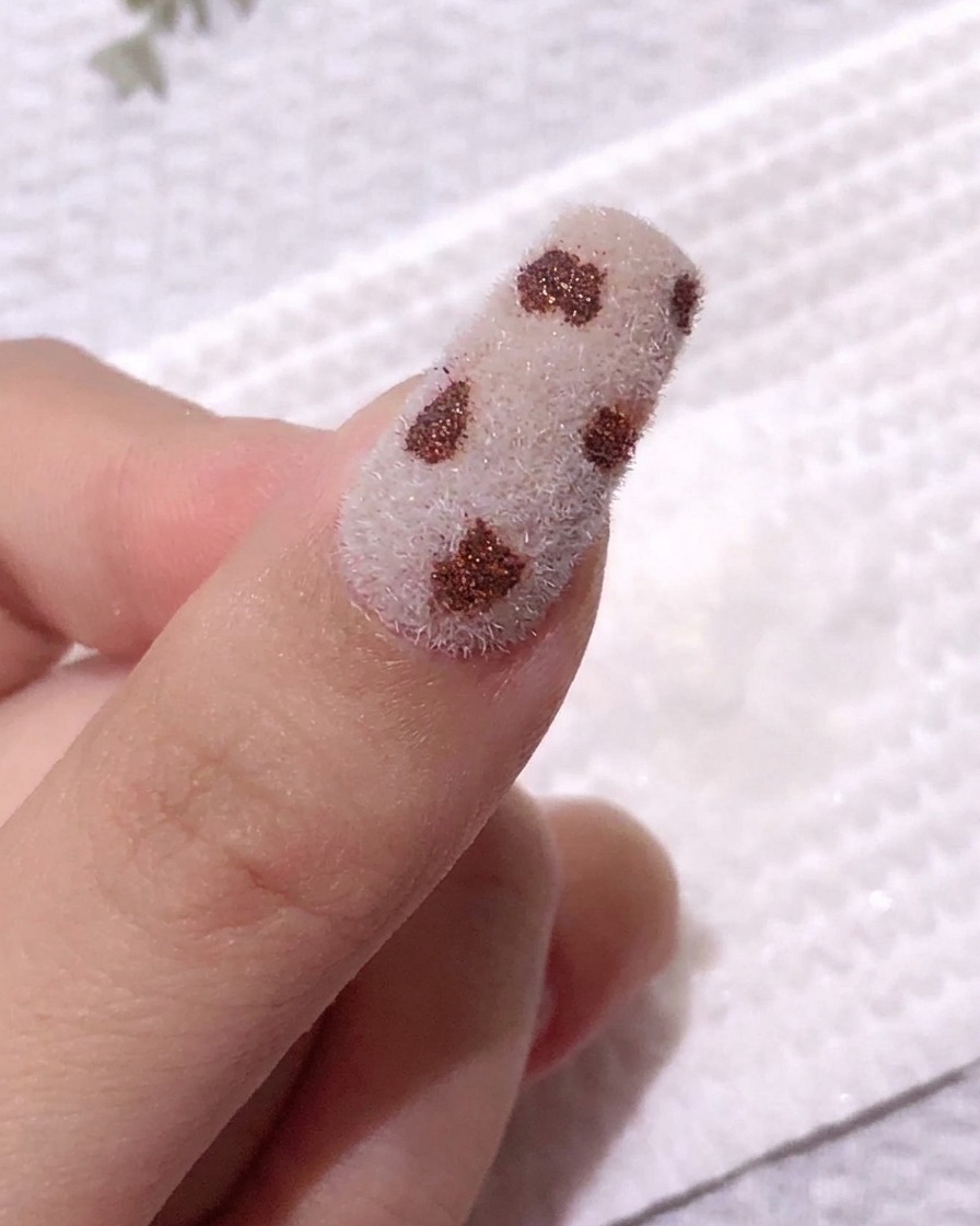 Un ongle présentant des taches café sur une surface en velours blanc, après un léger essuyage pour fixer le design.