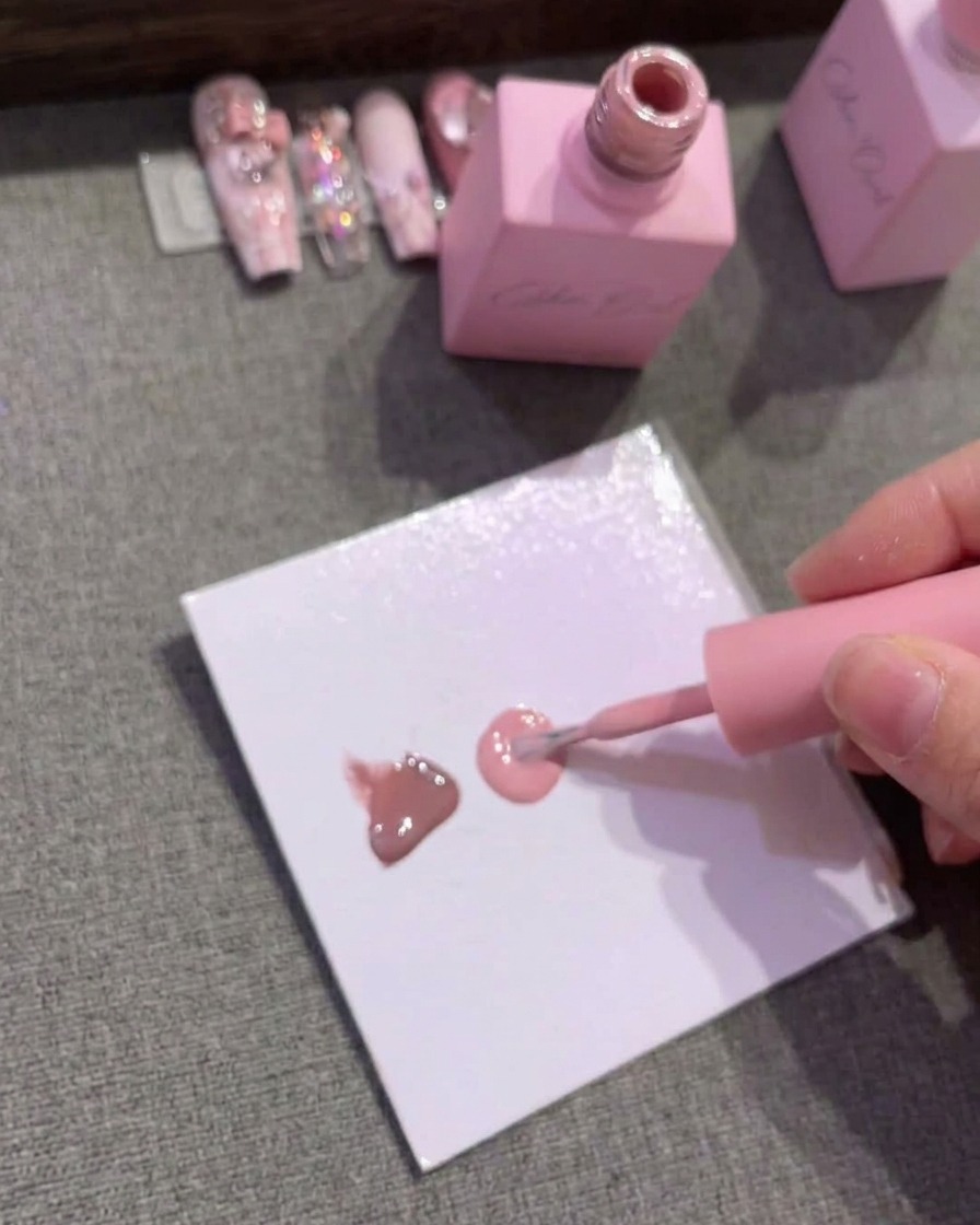 Papier palette montrant trois gouttes distinctes de vernis gel marron, rose moyen et rose clair.
