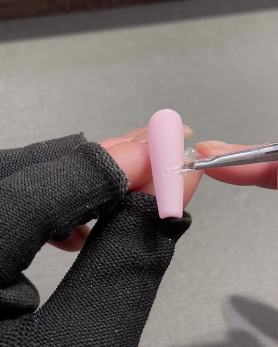 Un pinceau de détail fin appliquant du gel plaster blanc texturé pour créer une ligne de sourire french sur une base dongle rose.