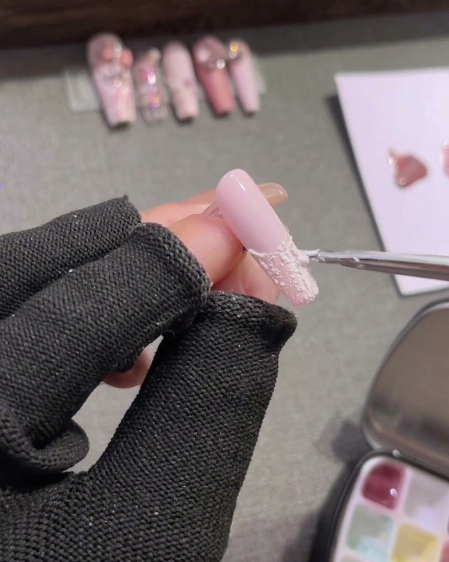 Un pinceau de détail remplissant le bout dun ongle rose avec du gel plaster blanc opaque.