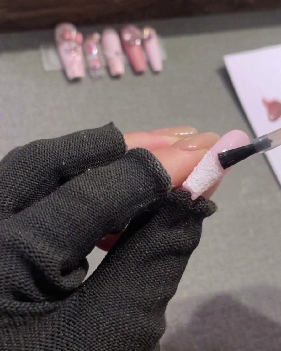 Un petit pinceau à ongles appliquant un top coat mat transparent sur la moitié supérieure rose dun ongle en amande, sarrêtant juste au-dessus dune french tip blanche texturée.