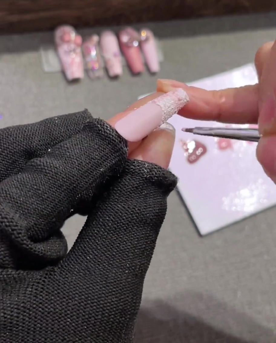 Un pinceau à ongles fin dessinant des lignes horizontales rose clair sur une pointe blanche texturée, entrecroisant les lignes verticales pour créer une grille.